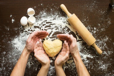 hands of men and women make dough heart. the symbols of protection, warmth and comfort. baking lovers on valentine's day