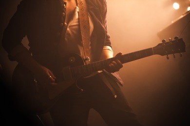 rock and roll music background, electric guitar player on a stage with warm scenic illumination, soft selective focus