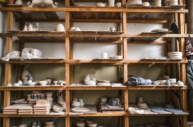 wooden racks in a pottery workshop in which there are pottery, many different pottery standing on the shelves in a potery workshop. low light