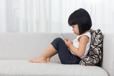 asian chinese little girl lying on the sofa with mobile phone in the living room at home.