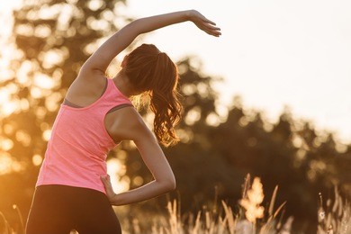 young female  stretching before fitness training session at the park. healthy young woman warming up outdoors. she is stretching her arms and looking away,hi key.