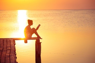 girl sitting on a pier and reading at the sunset time