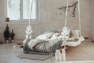 the bed suspended from the ceiling. grey big cozy blanket knit. scandinavian style, gray plaid, candles.