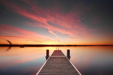 perspective view of a wooden pier on the pond at sunset with perfectly specular reflection