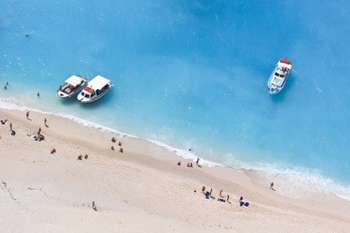 aerial view of a beach with some motorboats and some people swimming in the turquoise sea.
