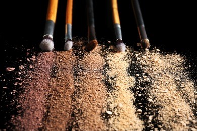 make up brushes and colourful eye shadows on black background