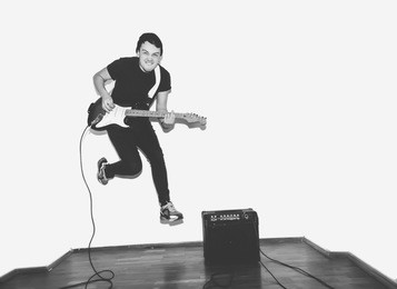 awesome crazy fashion young rock guitar player jumps with passion in studio. black and white toned. white background.