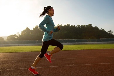 young woman running during sunny morning on stadium track