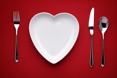 plate in shape of heart, table knife and fork on red 