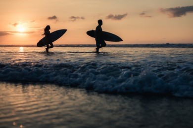 silhouette of a couple with surf boards at the beach sunset time