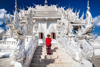 woman in red shirt in front of wat rong khun the white temple in chiang rai, thailand