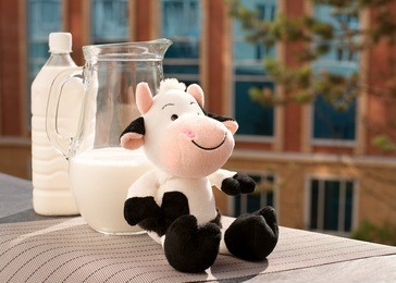 milk and toy cow. funny spotted cow against a background of milk. milk in a jug and a plastic bottle on the windowsill balcony. breakfast is good for health.