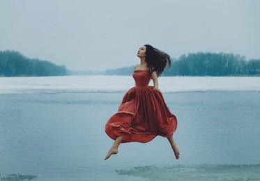 beautiful brunette girl jumping, walking in the air. background shore of a frozen river.  sad face with a glimmer of hope to escape from the routine of everyday life. fantasy photo, creative color.
