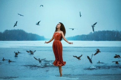 beautiful young brunette woman flies with the birds. background shore of a frozen river. . sad face with a glimmer of hope to escape from the routine of everyday life. fantasy photo, creative color