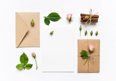 letter, envelope and a present in eco paper on white background. wedding invitation cards or love letter with pink roses. valentine's day or other holiday concept, top view, flat lay, overhead view