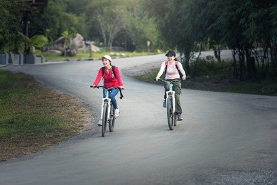 two stylish young female friends on a bicycle along road. best friends enjoying a day on bike.