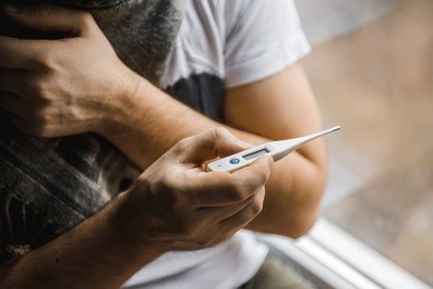 man feeling bad lying in the bed and looking the thermometer , main focus on the thermometer
