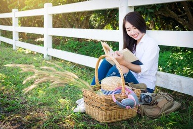 pretty relaxed young asian woman reading a book at the lawn garen with sun shining, vintage tone.