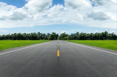 empty road through a green grass field in a summer day
