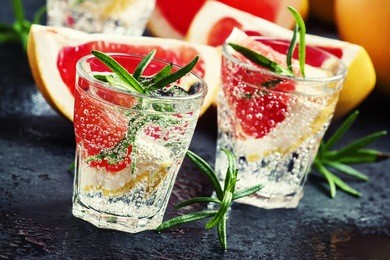 alcoholic cocktail with grapefruit, soda, ice, gin and rosemary, dark stone background, selective focus