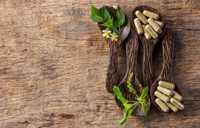 herbal capsules with herbs basil on wooden spoon 