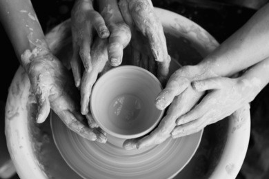 family working on pottery wheel. top view of mother, father and son hands making ceramic pot or sculpting clay
