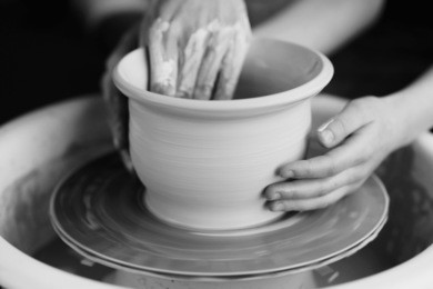 mother teaches son to work on pottery wheel. close up of dirty hands sculpting clay.