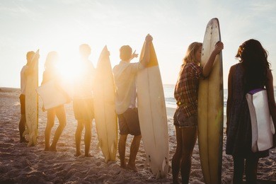 happy friends standing in line with surfboards on the beach