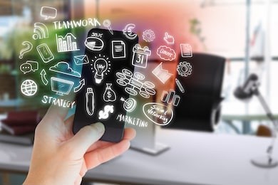 female hand holding a smartphone against blurry picture of computer on desk 3d