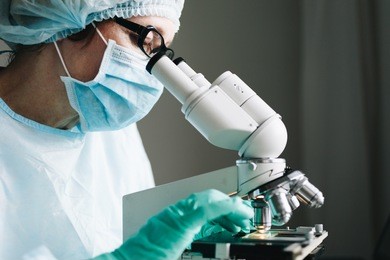 scientist in blue medical gloves and uniform learning samples with microscope in laboratory.