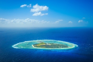 a aerial of a coral cay island surrounded by shallow reef and deep blue water
