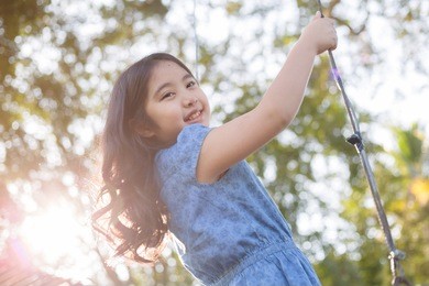 happy little asian girl playing swing outdoor in the park 
