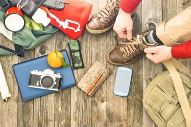 travel man tying boots for trekking day top view of items for hiking and adventure - active male hands on shoelaces above angle with camera mobile phone and backpack on old wooden floor background