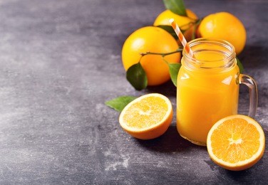 glass jar of fresh orange juice with fresh fruits on dark table.