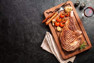 succulent grilled tomahawk beef steak on the bone with seasonings, fresh rosemary and grilled vegetables on a black background, top view