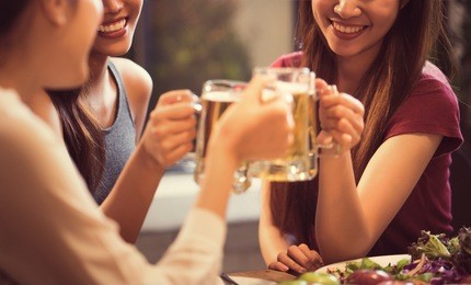 women are drinking beer and the clink glasses in a restaurant.