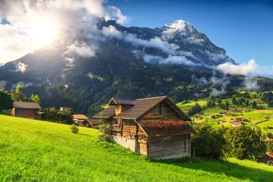 fabulous alpine wooden houses, green fields and famous touristic grindelwald town with high north face of eiger mountains, bernese oberland, switzerland, europe