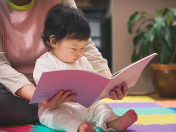 asian baby girl reading book with mom