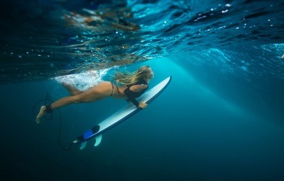 a blonde slim girl doing duck dive under blue wave. water ripples under ocean surface. water sport activity in vacation. sea fun lessons and beachlife lifestyle.