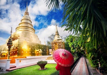 woman tourist with red traditional thai umbrella near golden stupa at temple wat phra singh in chiang mai, thailand