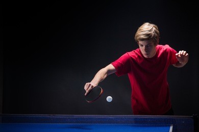 young man tennis player in play on black background