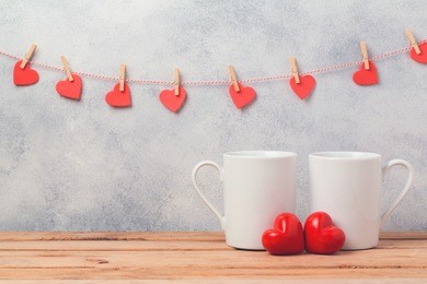 valentines day concept with white coffee cups and heart shapes over rustic background with garland