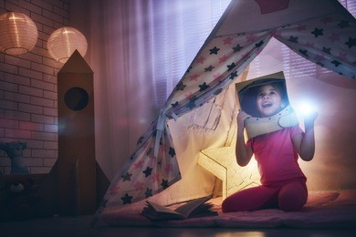 child in an astronaut costume with toy rocket playing and dreaming of becoming a spacemen. happy kid plays in tent. funny lovely girl having fun in children room. 