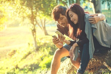 a man hugging a woman , sitting and using smartphones with feeling love in nature outdoor park