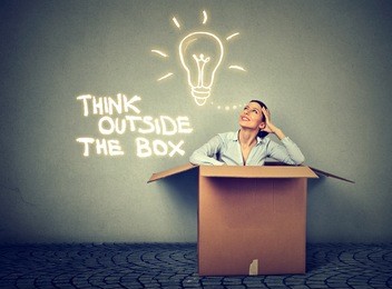 think outside the box concept. young woman coming out of box with great bright idea light bulb isolated on gray wall background 