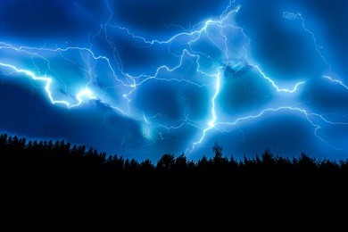 lightning strike on a dark blue sky over the forest silhouette