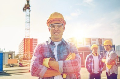 business, building, teamwork and people concept - group of smiling builders in hardhats at construction site