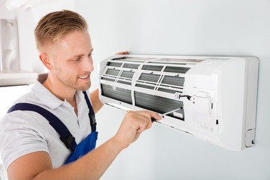 happy male technician repairing air conditioner with screwdriver