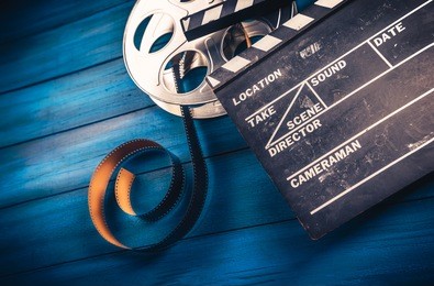 35mm film, reel and movie clapper with dramatic lighting on a wooden background