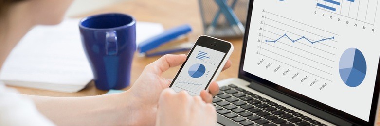 close-up rear view of business woman working in office on pc holding smartphone and looking at screen with diagrams, using mobile phone and laptop. horizontal photo banner for website header design